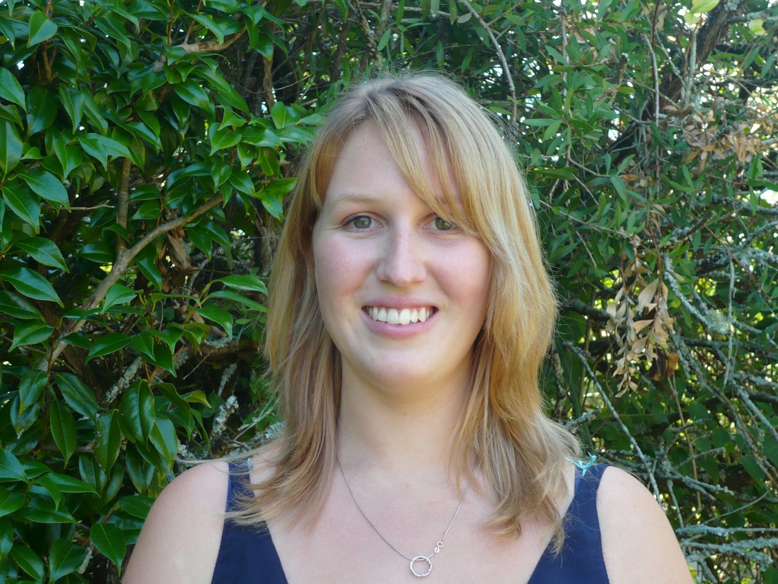 Nikki Webb: head and shoulder view with bush behind her.