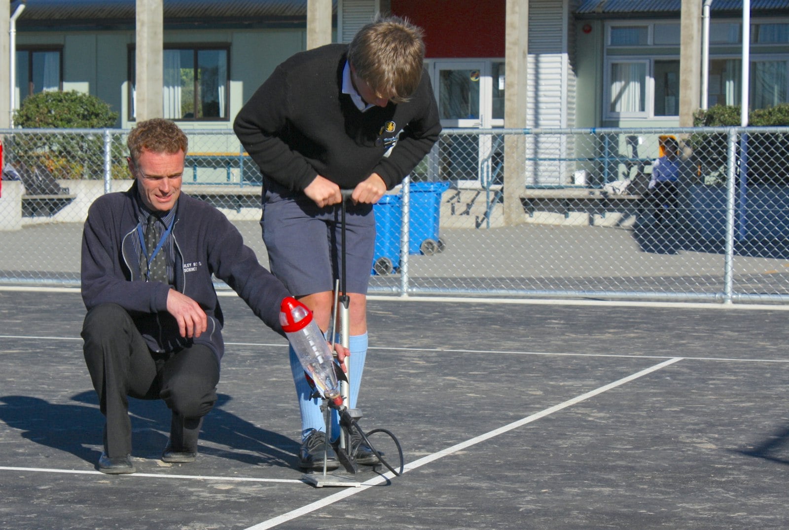 Teacher and student testing a water bottle rocket outside.